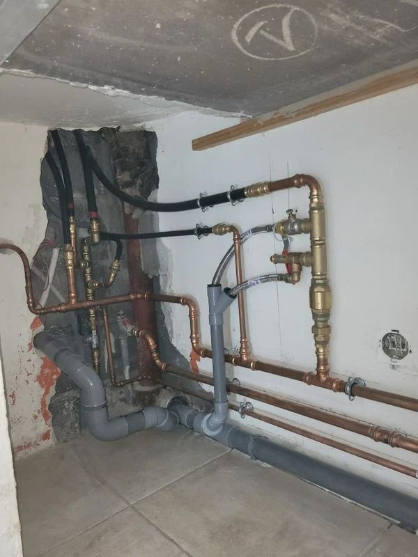 Tuyaux et accessoires de plomberie, y compris les tuyaux en cuivre et en PVC, installés sur un mur.