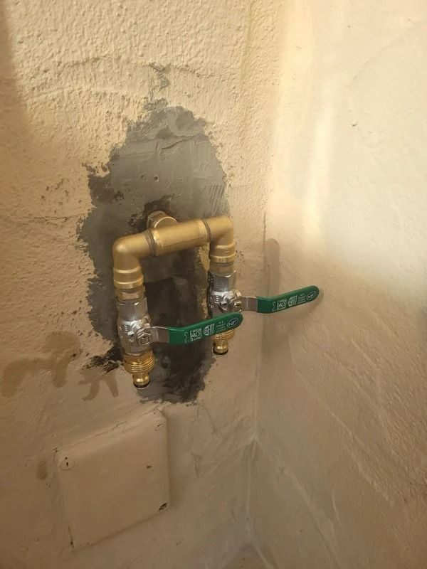 Tuyauterie en laiton avec deux robinets à poignée verte montés sur un mur texturé.