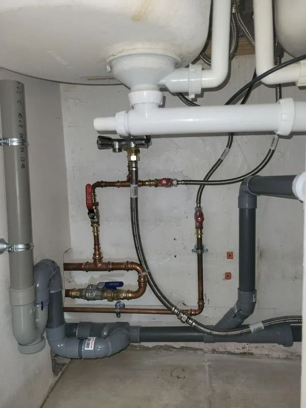 Tuyauterie et accessoires de plomberie sous un évier. Tuyaux gris et en cuivre avec vannes d'arrêt et siphons.