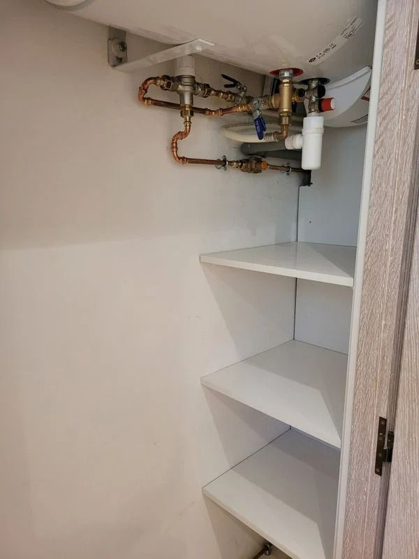 Placard blanc avec étagères et tuyaux en cuivre.