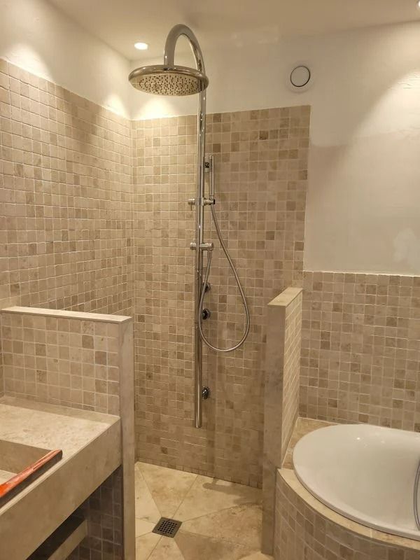 Cabine de douche avec murs en mosaïque, pommeau de douche effet pluie et petite baignoire circulaire.