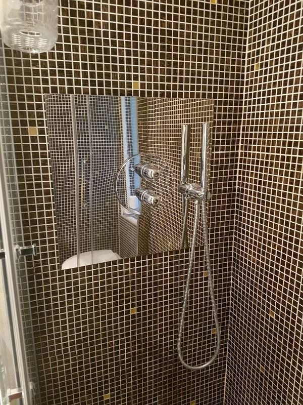 Douche avec carrelage mosaïque marron, étagère encastrée avec robinet et pommeau de douche.