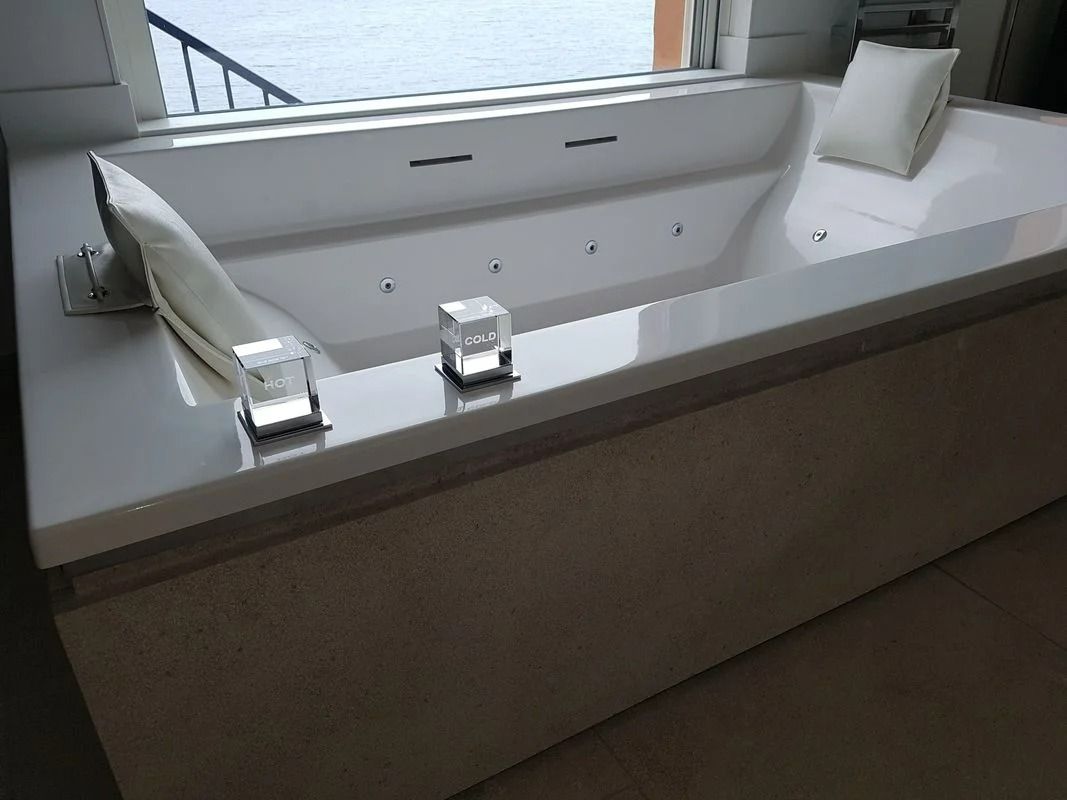 Baignoire jacuzzi blanche avec jets, bougies et oreiller près d'une fenêtre.