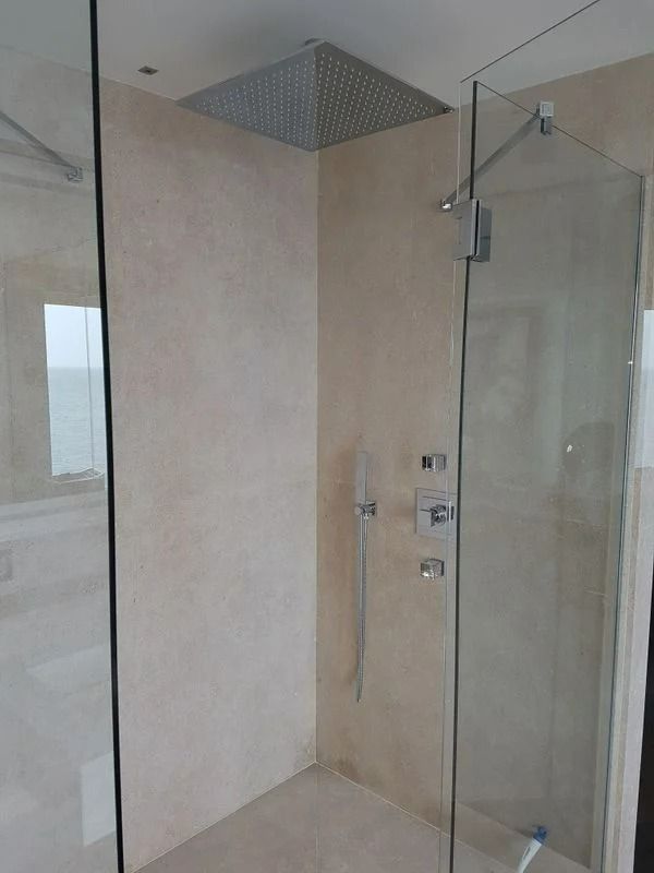 Douche moderne avec porte en verre, pommeau de douche carré effet pluie, murs beige clair et robinetterie chromée.