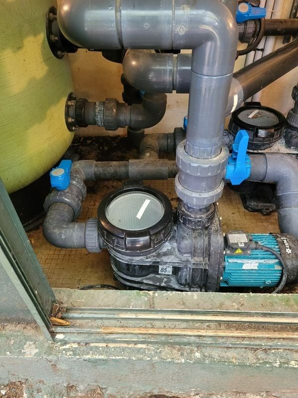 Pompe de piscine avec tuyaux en PVC gris, vannes bleues et moteur turquoise.