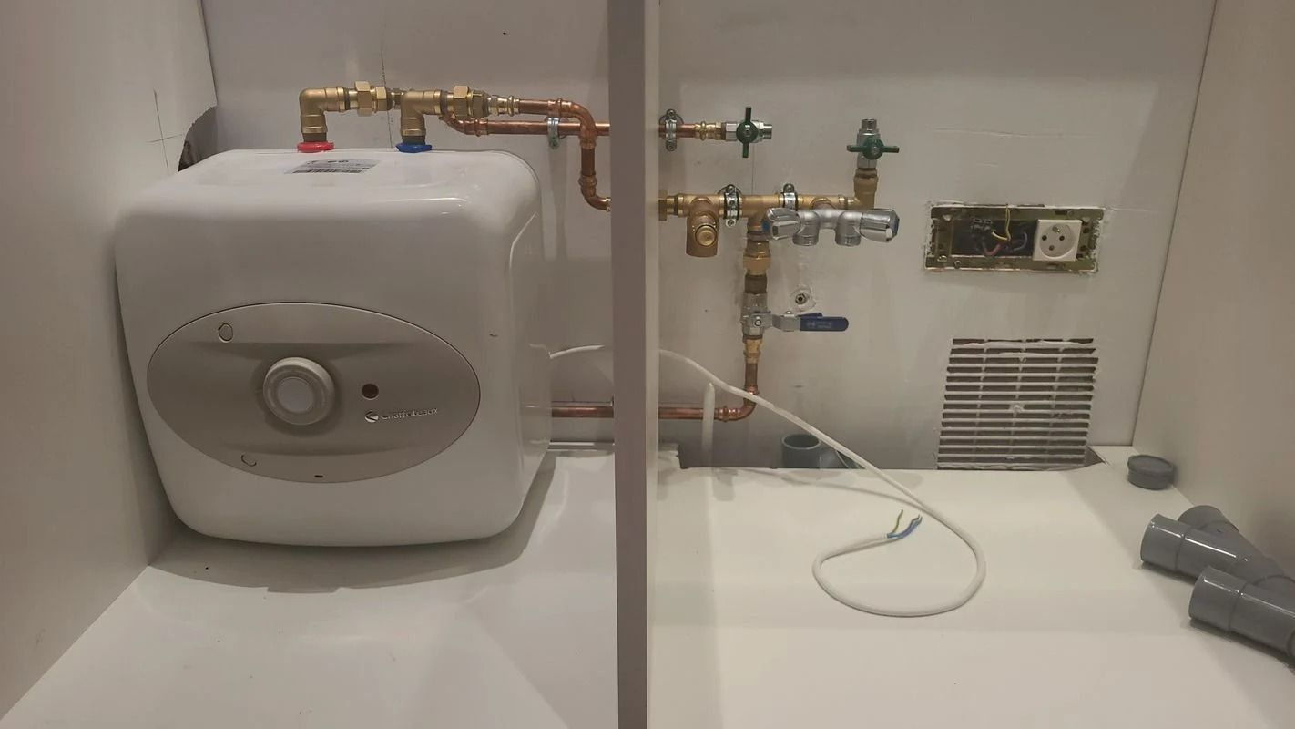 Chauffe-eau électrique blanc et tuyauterie en cuivre à l'intérieur d'un meuble blanc.