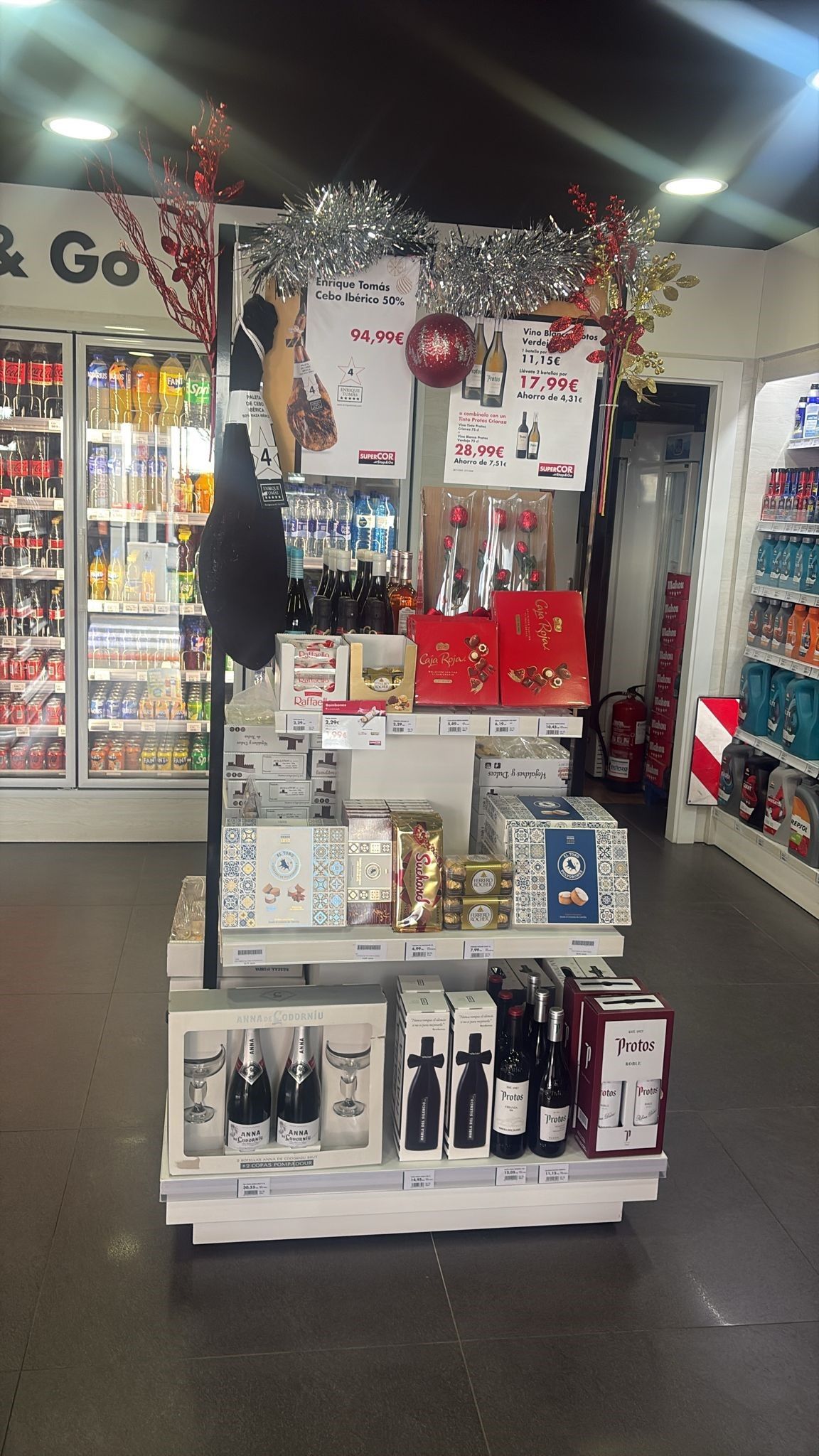 Exhibición de cajas de vino y regalos en una tienda, decoradas con adornos y luces navideñas.