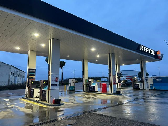 Gasolinera Repsol al anochecer. El pavimento mojado refleja las luces. Surtidores de gasolina bajo una marquesina.