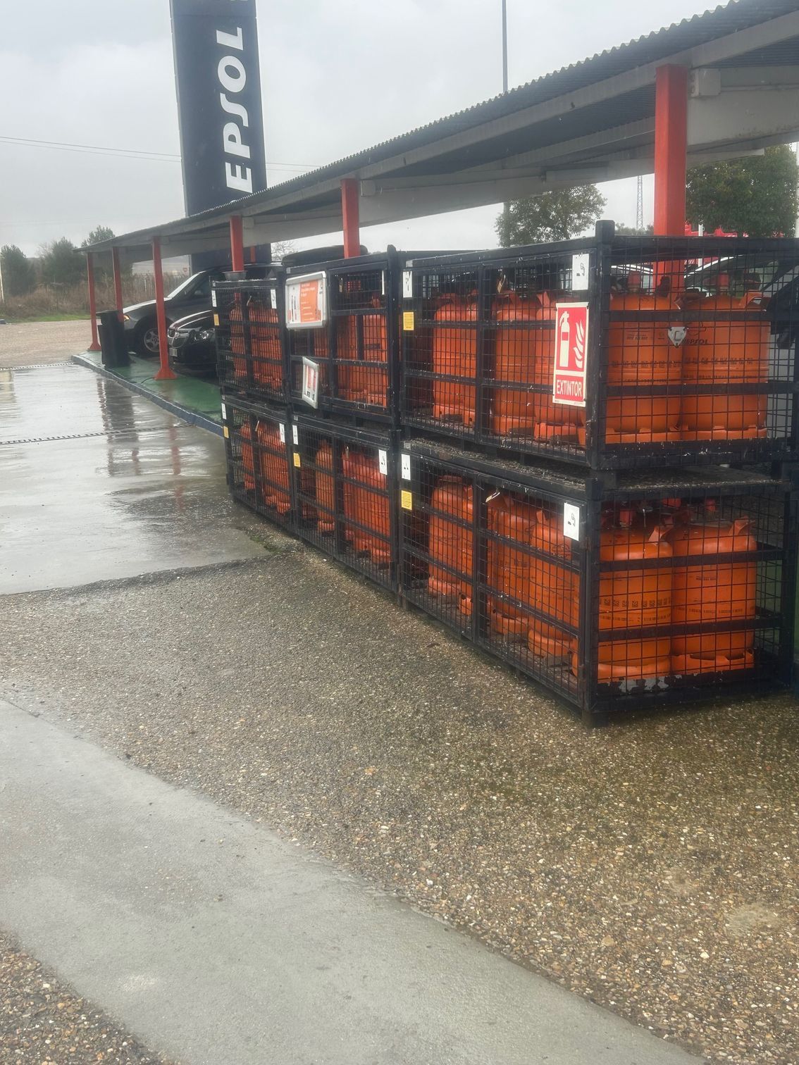 Tanques de propano naranjas en jaulas negras en una gasolinera al aire libre, bajo una marquesina. Cartel de la EPSOL al fondo.