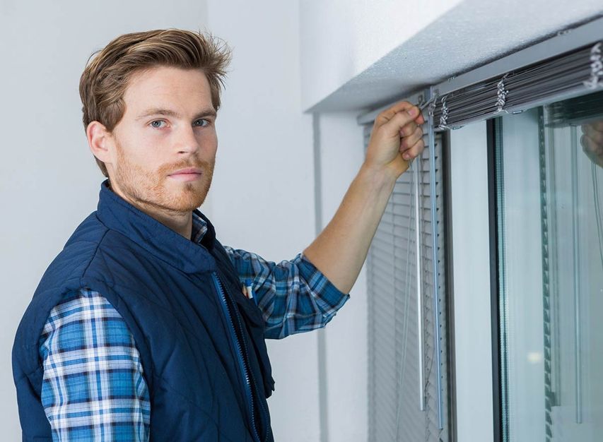 Un hombre está instalando persianas en una ventana.
