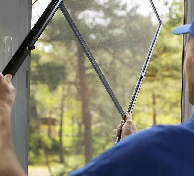 Un hombre con una camisa azul está instalando una mosquitera en una ventana.