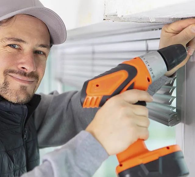 Un hombre está usando un taladro para instalar persianas en una ventana.