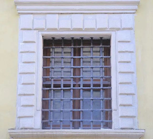 Una ventana con reja de hierro forjado en un edificio amarillo.