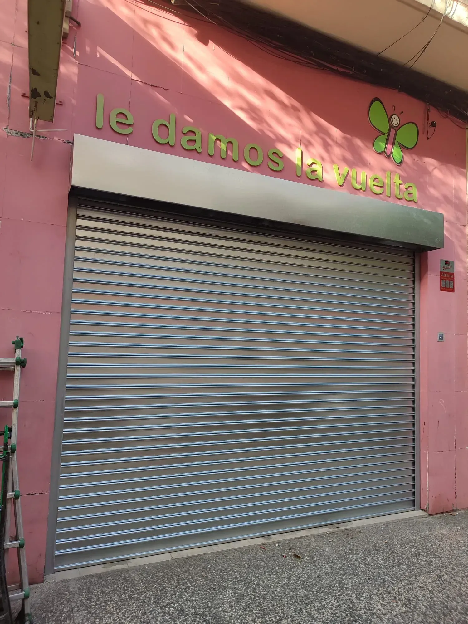 Un escaparate con una pared rosa y una persiana metálica.