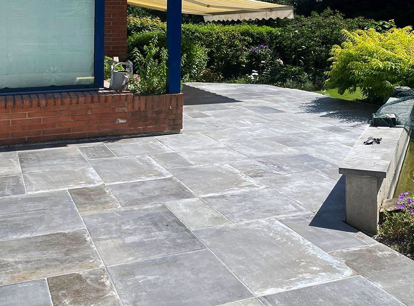 Terrasse pavée de dalles de pierre bleu-gris ; un mur de briques orné de plantes et de verdure, et un jardin avec un mur en arrière-plan.