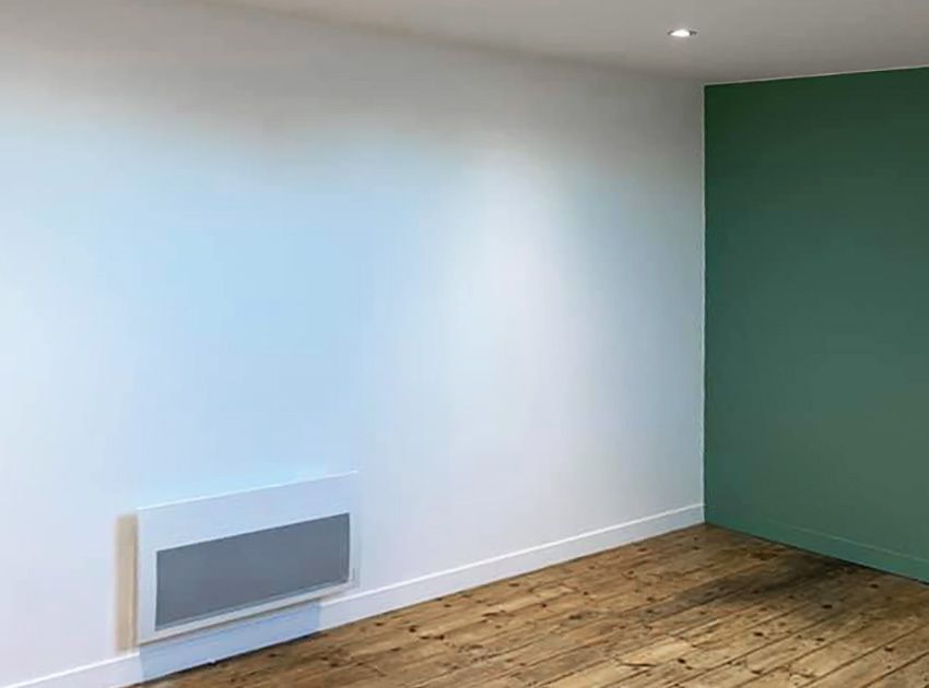 Pièce vide aux murs blancs et verts, parquet et radiateur blanc.