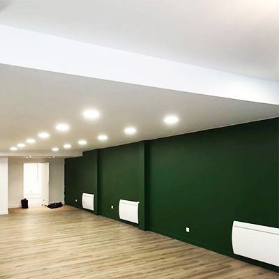 Pièce vide aux murs verts, plafond blanc, spots encastrés et parquet ; trois radiateurs blancs.