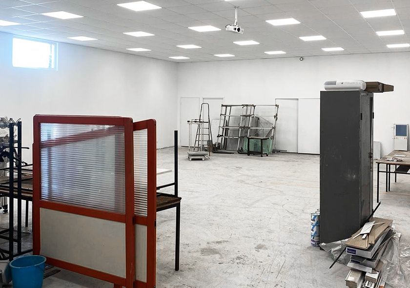 Pièce vide et lumineuse, avec des murs blancs, des plafonniers et quelques équipements en arrière-plan.