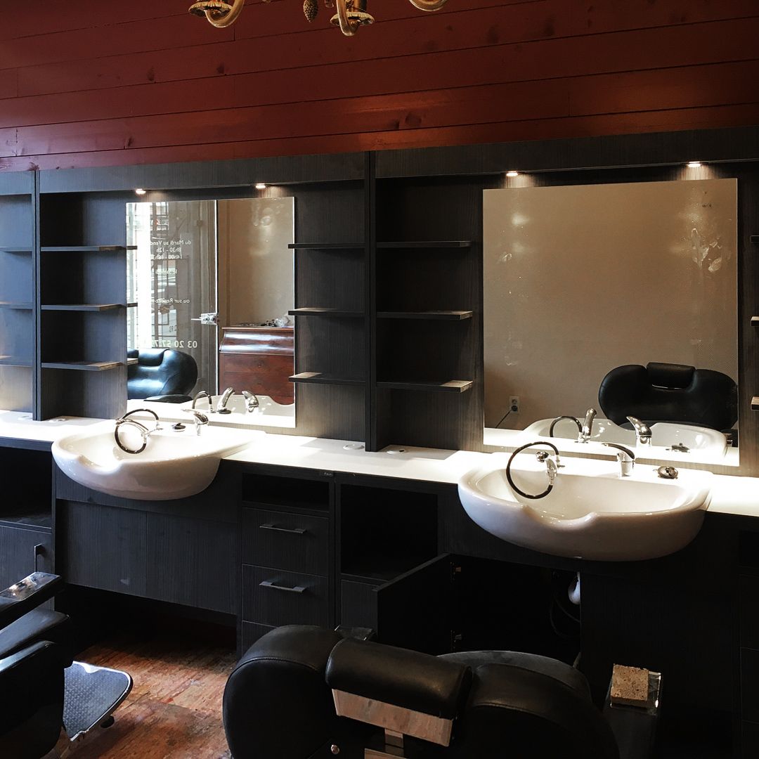 Intérieur d'un salon de coiffure avec meubles noirs, miroirs, lavabos et chaises. Plafond rouge.