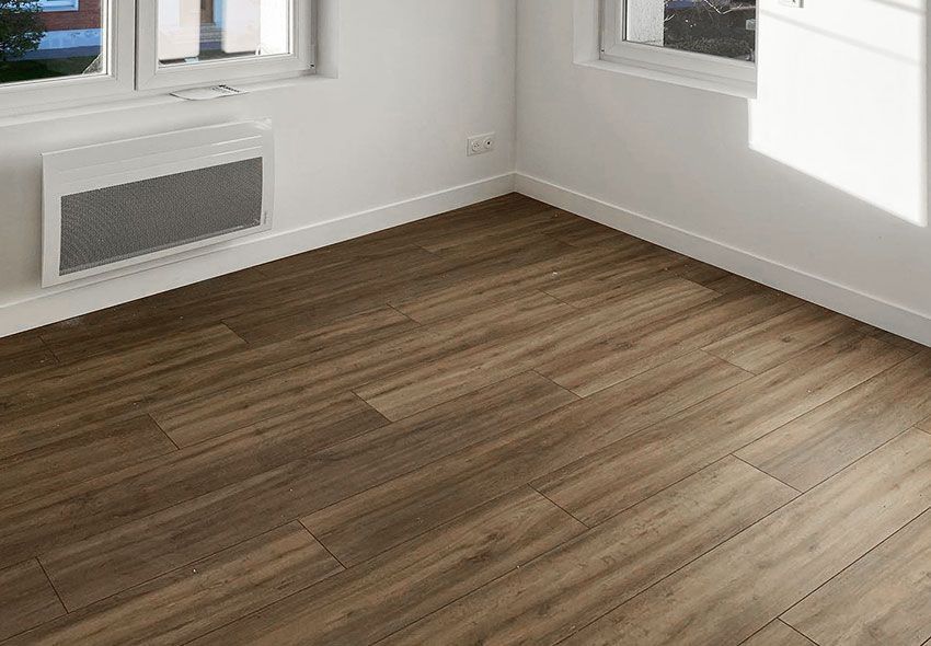 Pièce vide avec un sol imitation bois, des murs blancs et un radiateur mural sous une fenêtre.