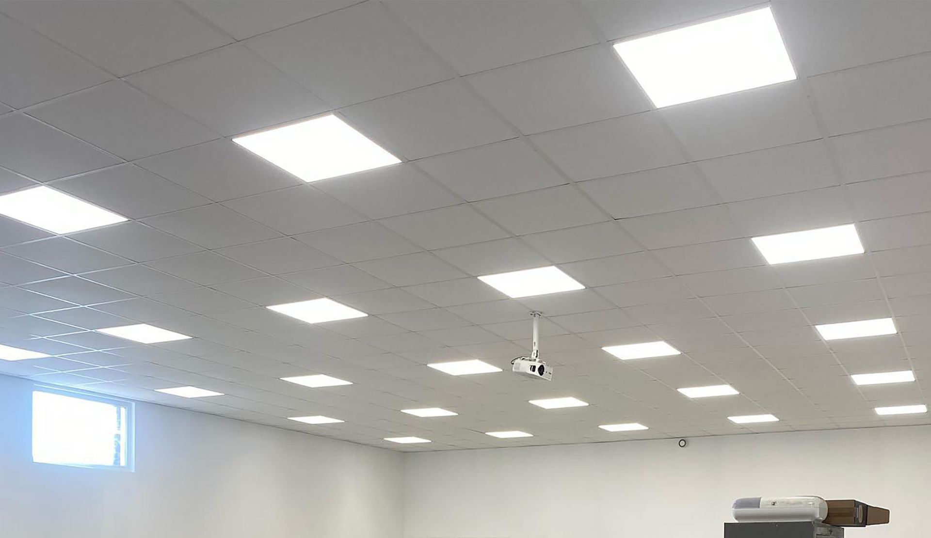Plafond blanc avec spots carrés et caméra de sécurité, dans une grande pièce.