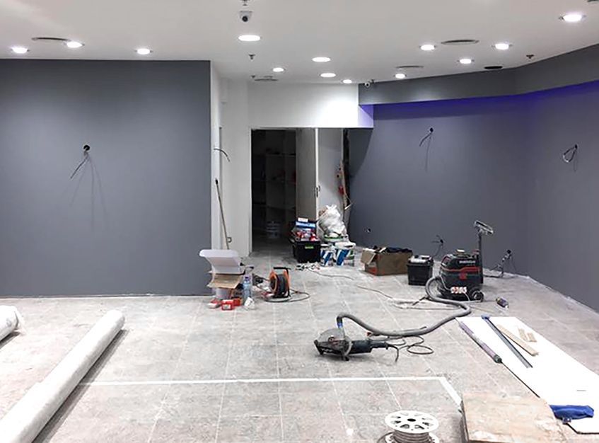 Intérieur d'un espace en rénovation, avec des murs gris, des débris de construction et des outils éparpillés sur le sol.