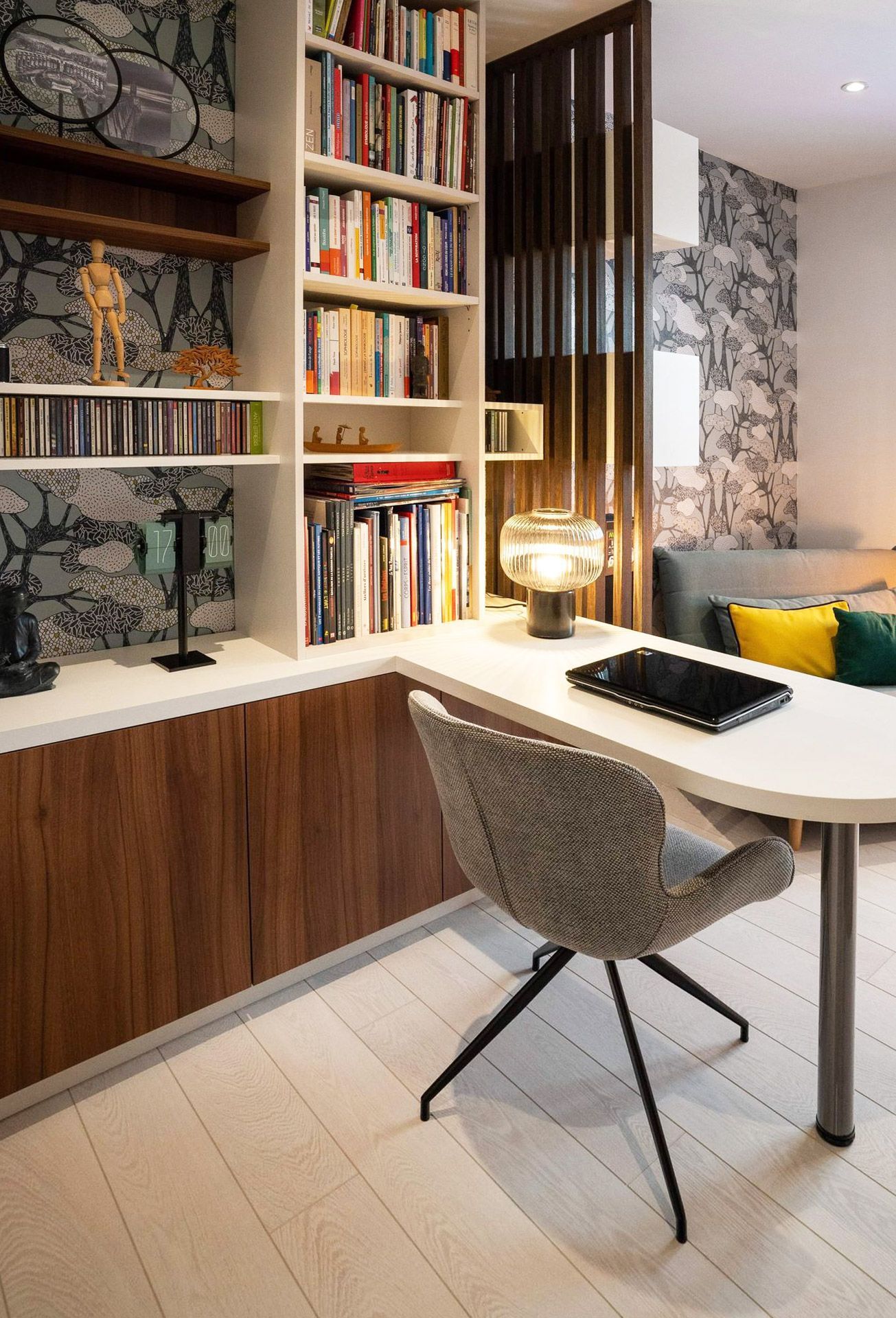 Bureau à domicile avec bibliothèque intégrée, bureau et chaise grise. Design moderne avec des touches de bois et de blanc.