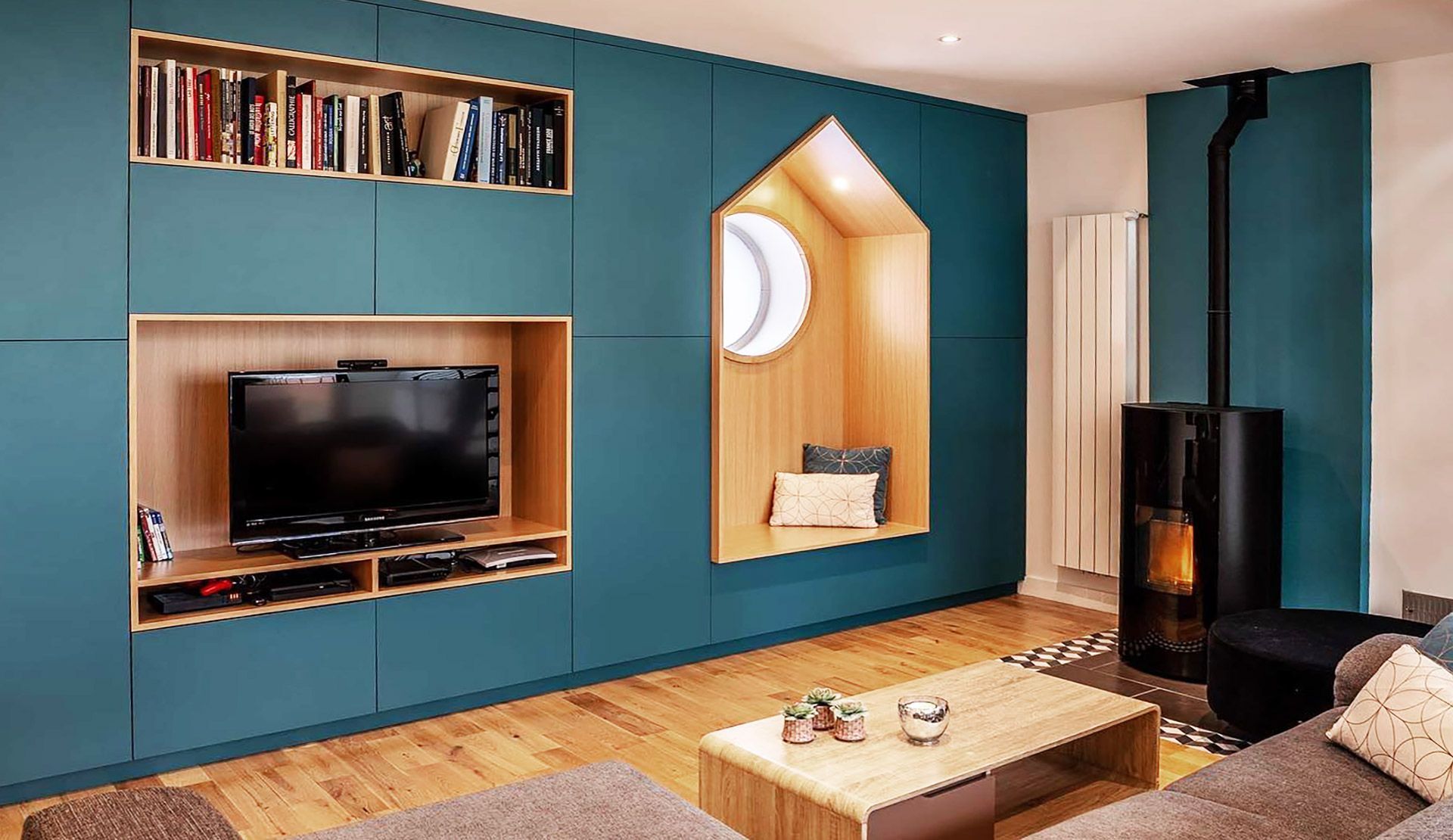 Mur d'accent bleu sarcelle avec télévision intégrée, bibliothèque et coin lecture. Parquet et cheminée moderne.