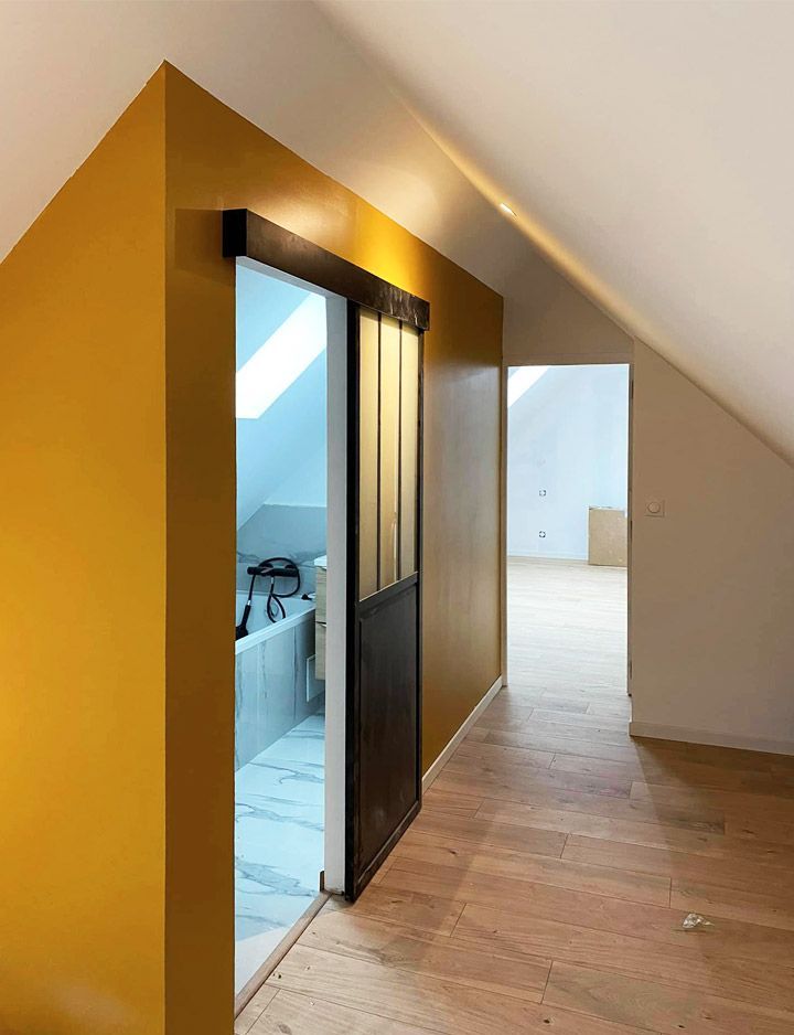 Pièce aux murs dorés avec une porte coulissante donnant sur une salle de bains. Une autre porte ouvre sur une pièce au parquet clair.