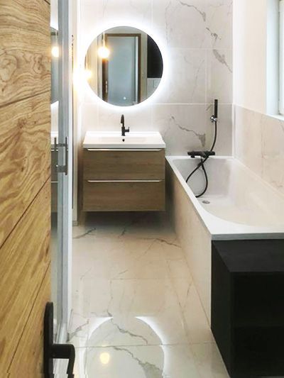 Salle de bains moderne avec carrelage imitation marbre, miroir rond éclairé, meuble-lavabo en bois et baignoire.