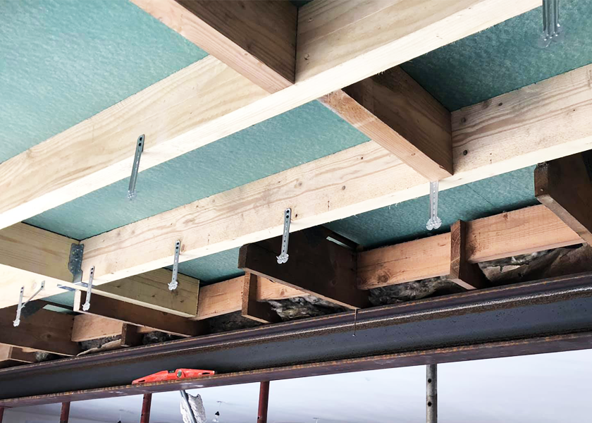 Poutres en bois et isolation installées au plafond, soutenues par des supports métalliques, vues d'en dessous.