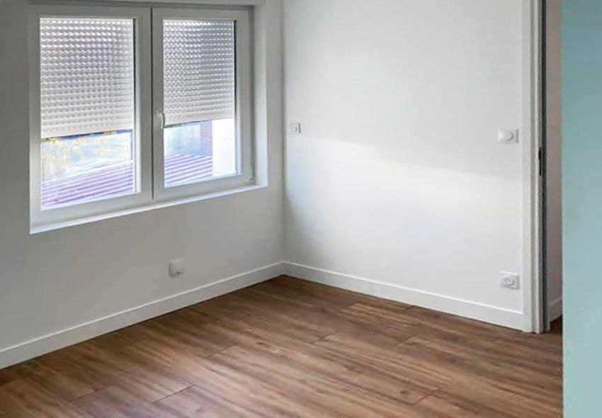 Pièce vide avec murs blancs, fenêtre et sol imitation bois.