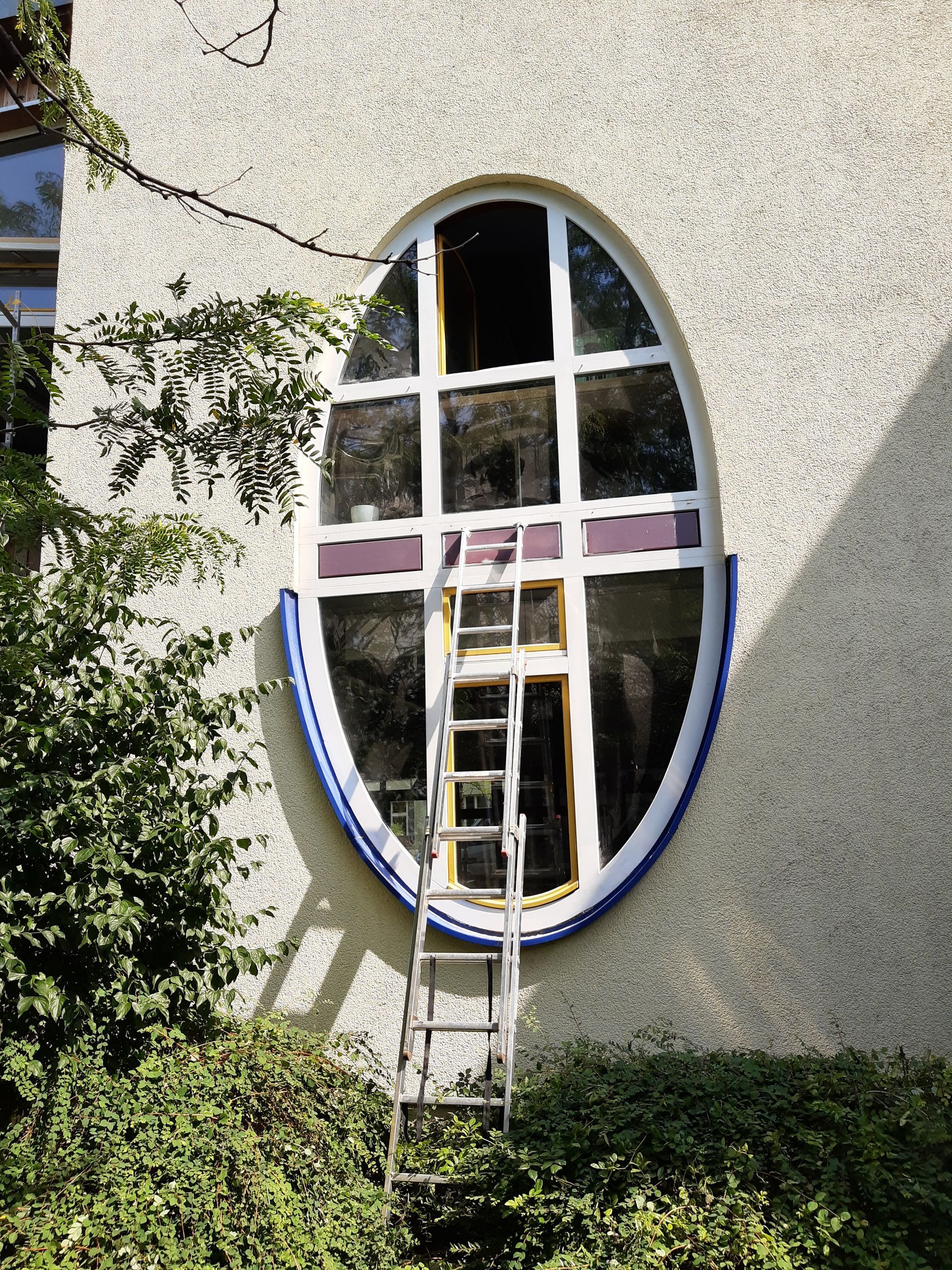 An einem großen ovalen Fenster eines Gebäudes ist eine Leiter befestigt