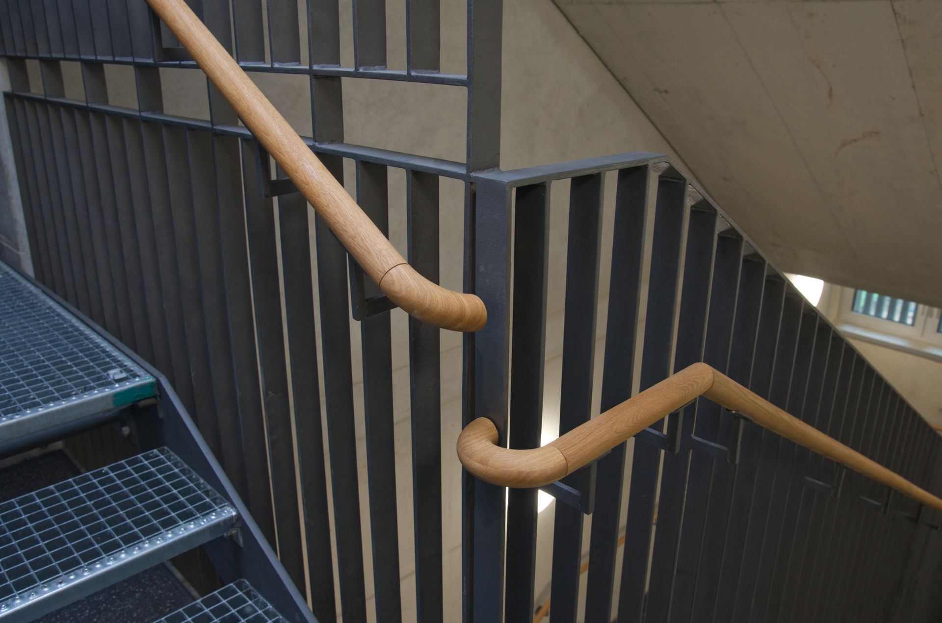 Innentreppe mit dunklem Metallgeländer und hellem Holzhandlauf.