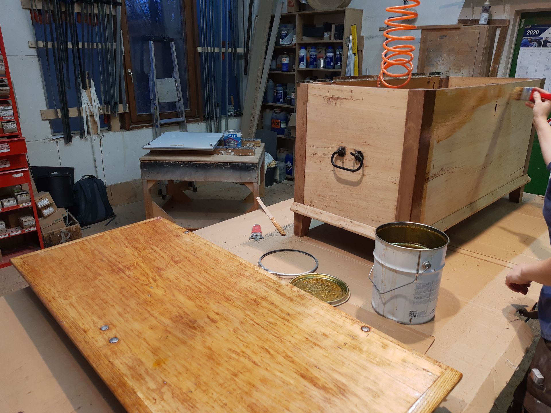 Eine Person bemalt einen Holztisch in einer Werkstatt.