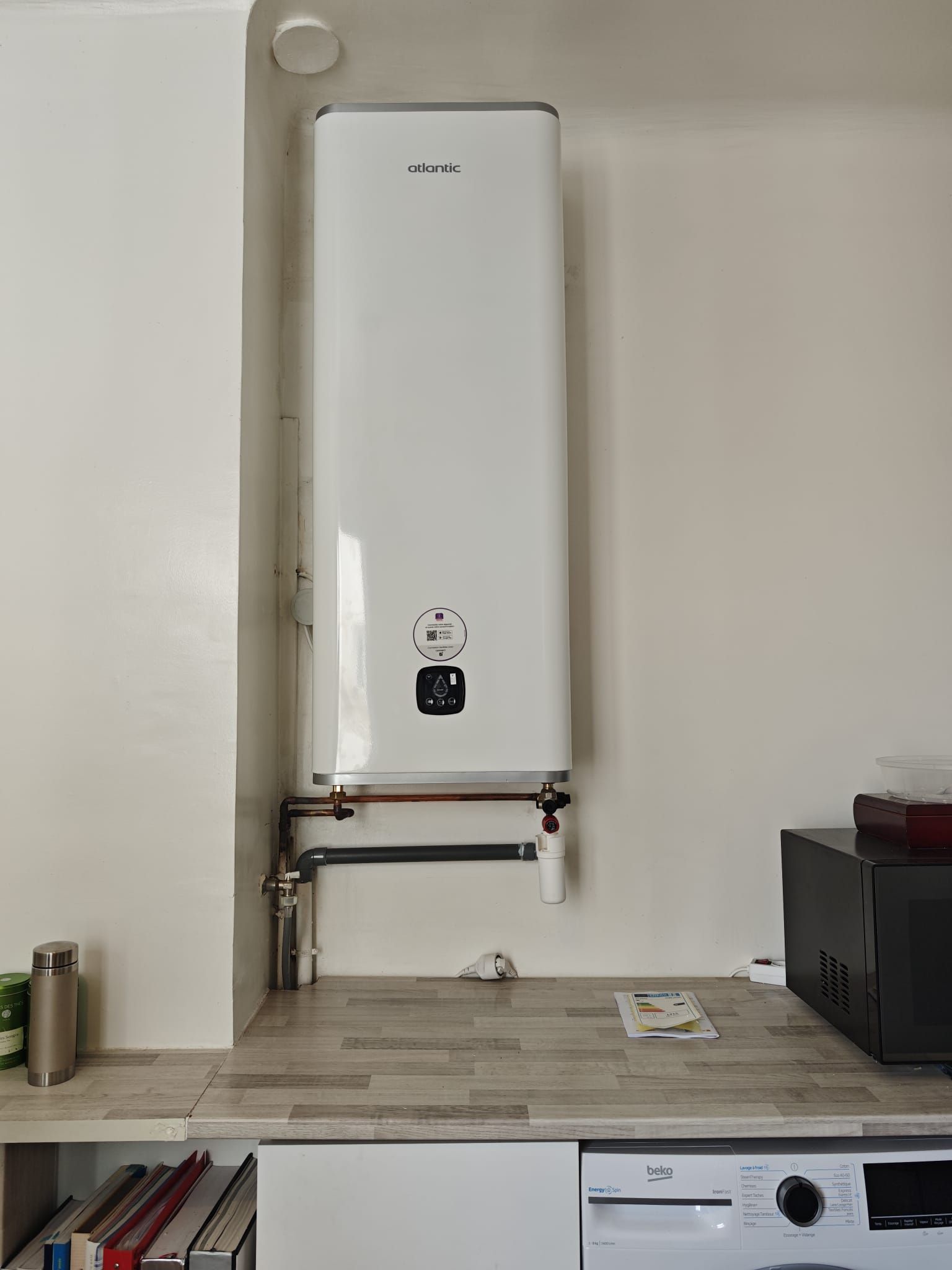 Chauffe-eau blanc fixé sur un comptoir de cuisine, la tuyauterie étant visible.