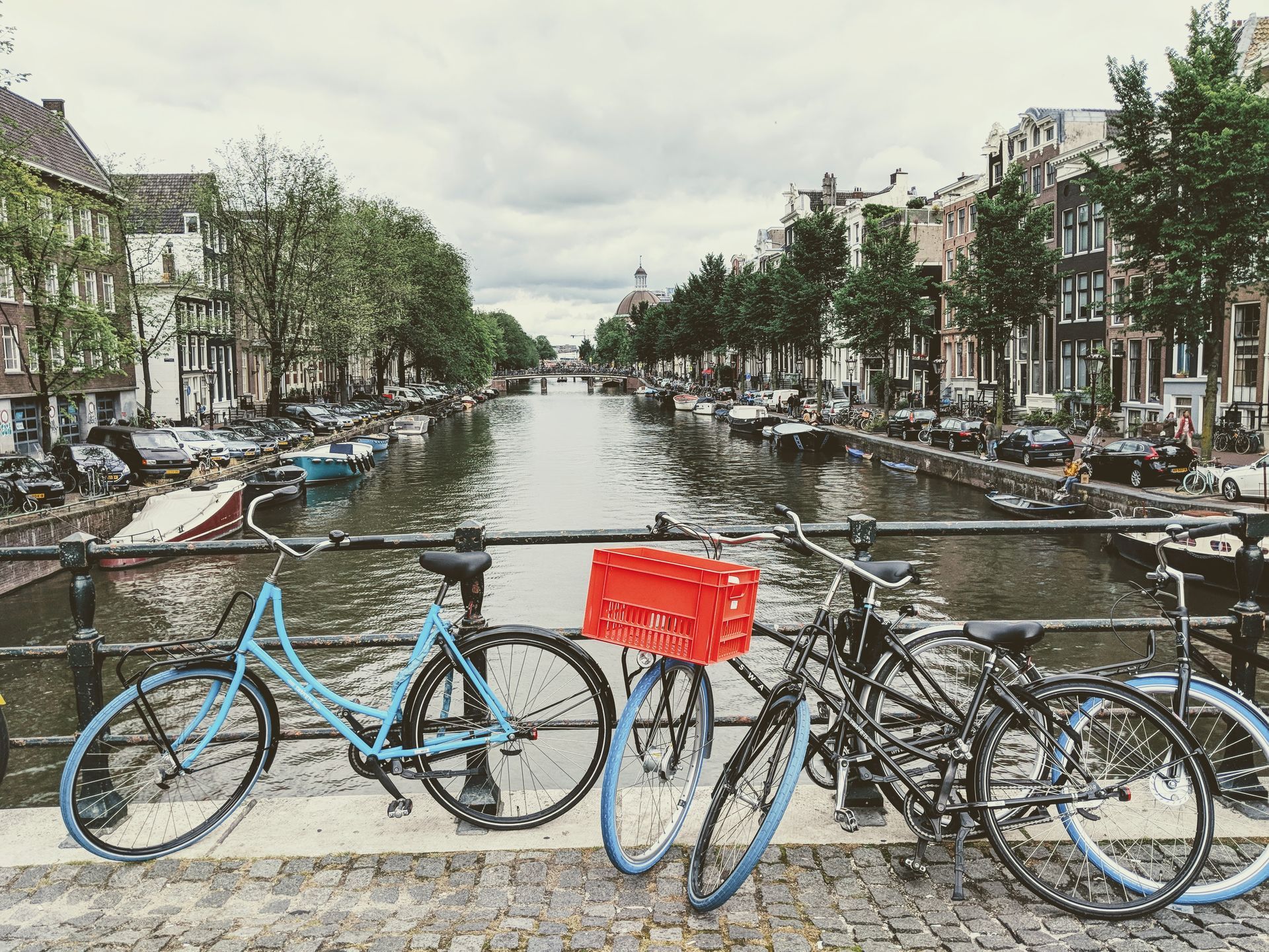 Fahrräder parken auf einer Brücke über einen Kanal in Amsterdam, Niederlande. Gebäude säumen das Wasser. Bewölkter Himmel.
