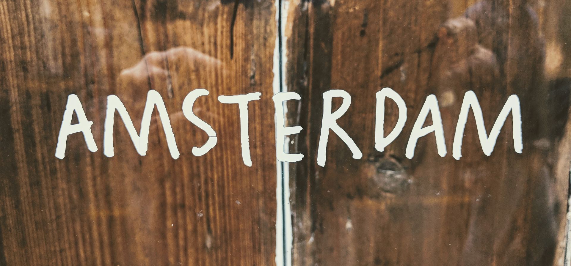 „Amsterdam“ in weißer Handschrift auf einer Holztür.