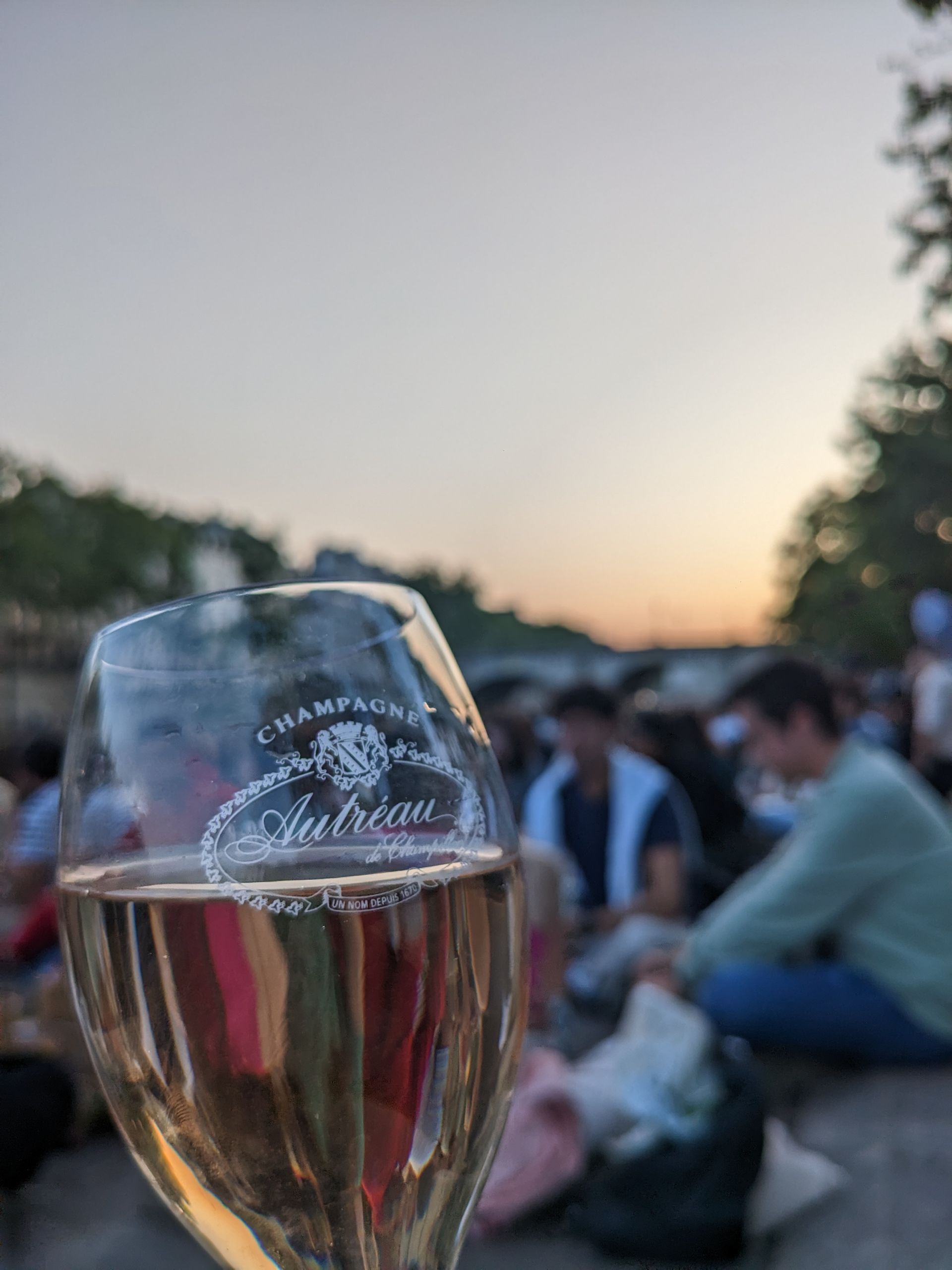 Ein Glas Prosecco. Im Hintergrund das Seine-Ufer bei Sonnenuntergang.