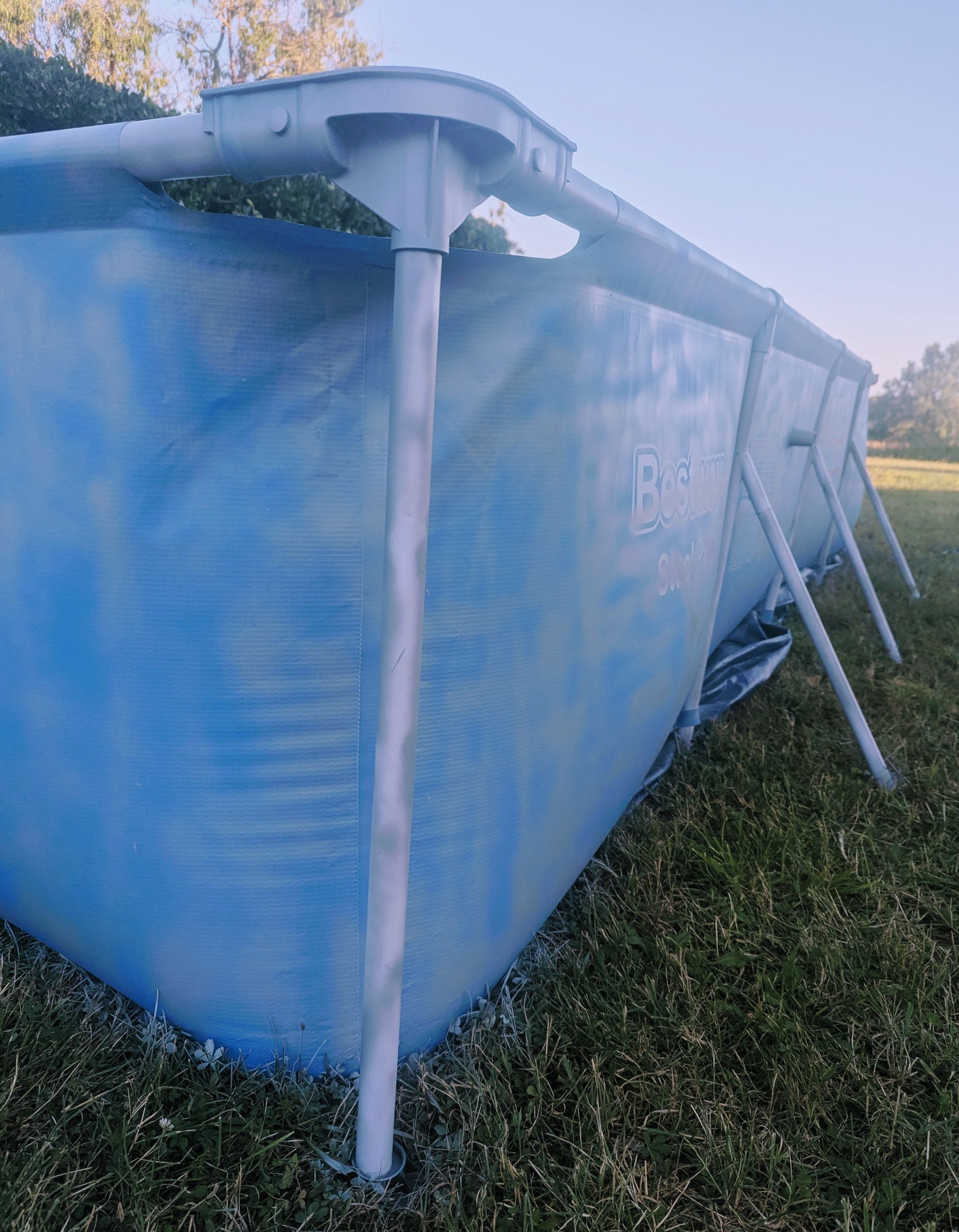 Blauer rechteckiger Aufstellpool mit Metallrahmen auf einer Rasenfläche.