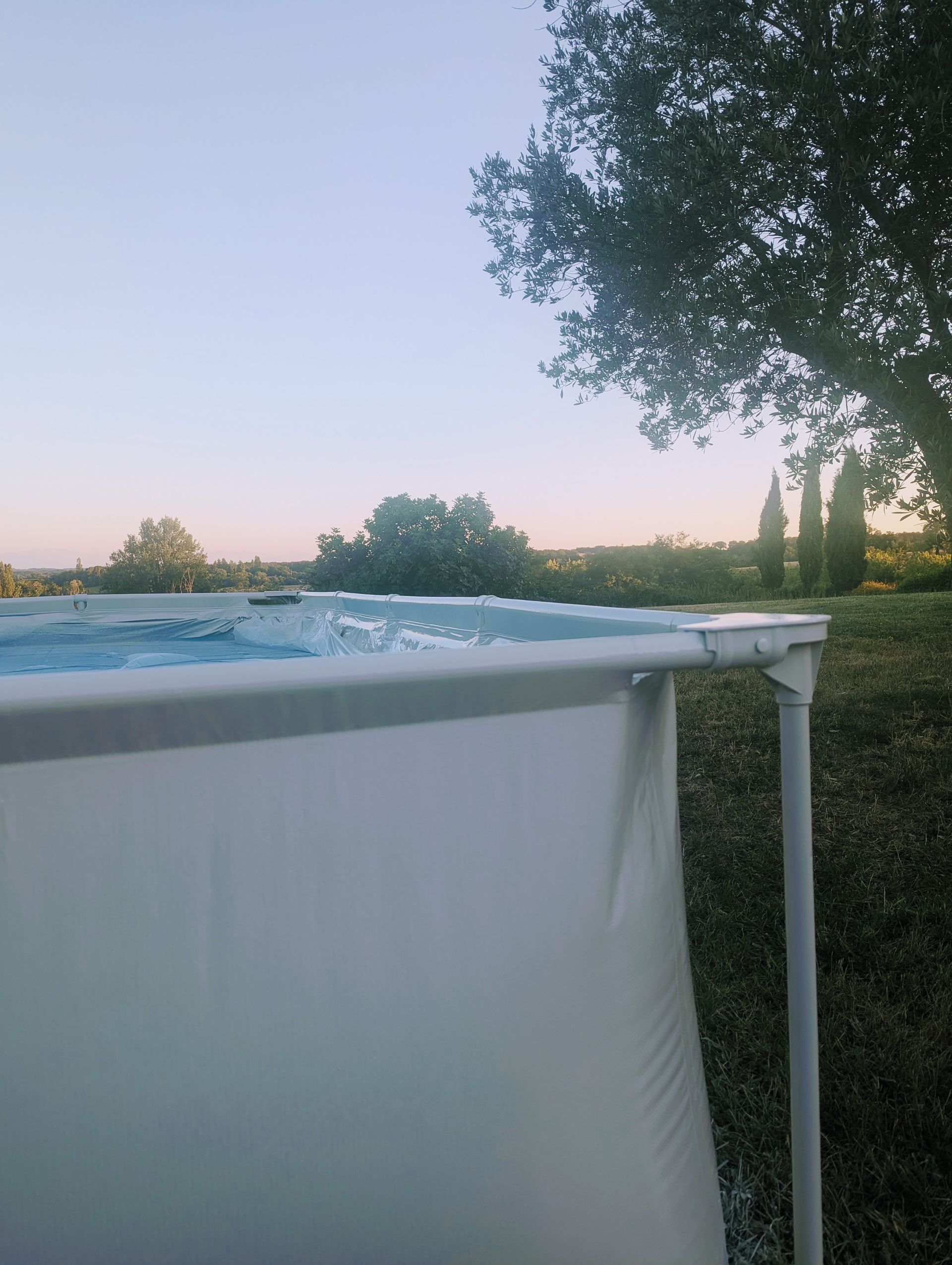 Aufstellpool mit Wasser gefüllt; grünes Gras und Bäume unter einem hellblauen Himmel.