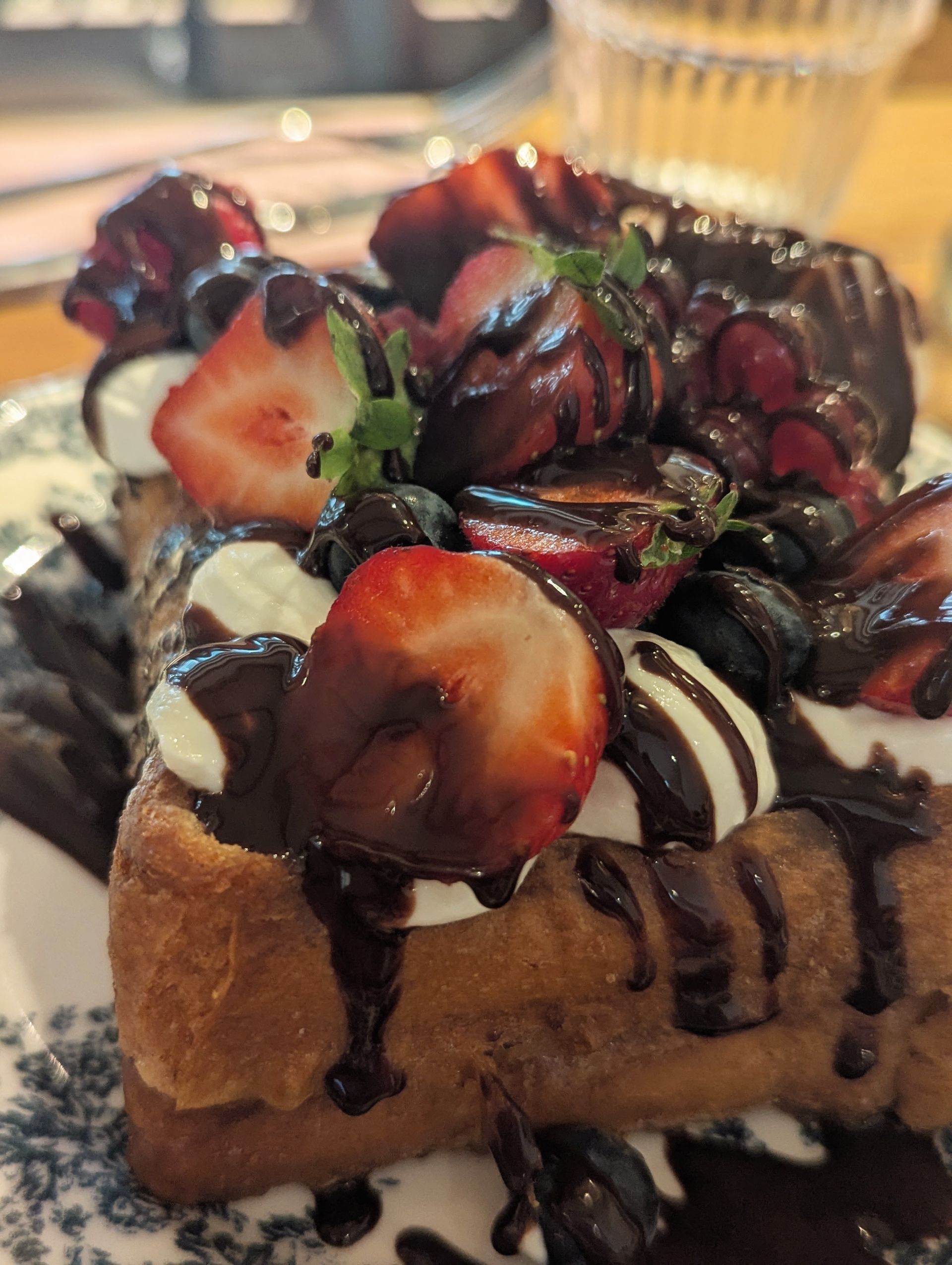 Waffel mit Erdbeeren, Blaubeeren, Schlagsahne und Schokoladensauce auf einem gemusterten Teller. REE7 Amsterdam.