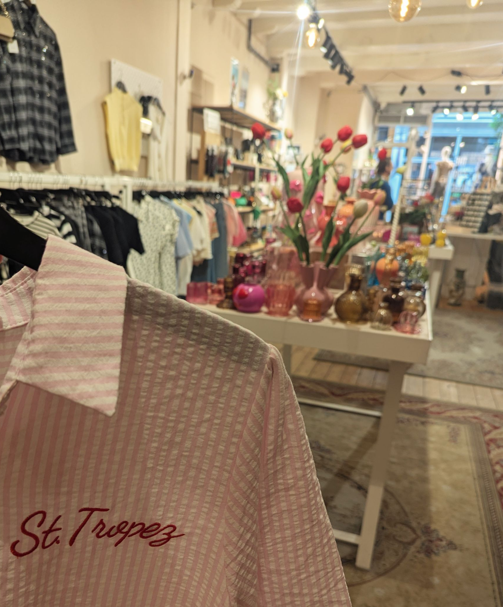 Rosa Hemd mit der Aufschrift „St. Tropez“ in einem Geschäft mit Kleidung, Dekorationen und unscharfem Hintergrund. Amsterdam