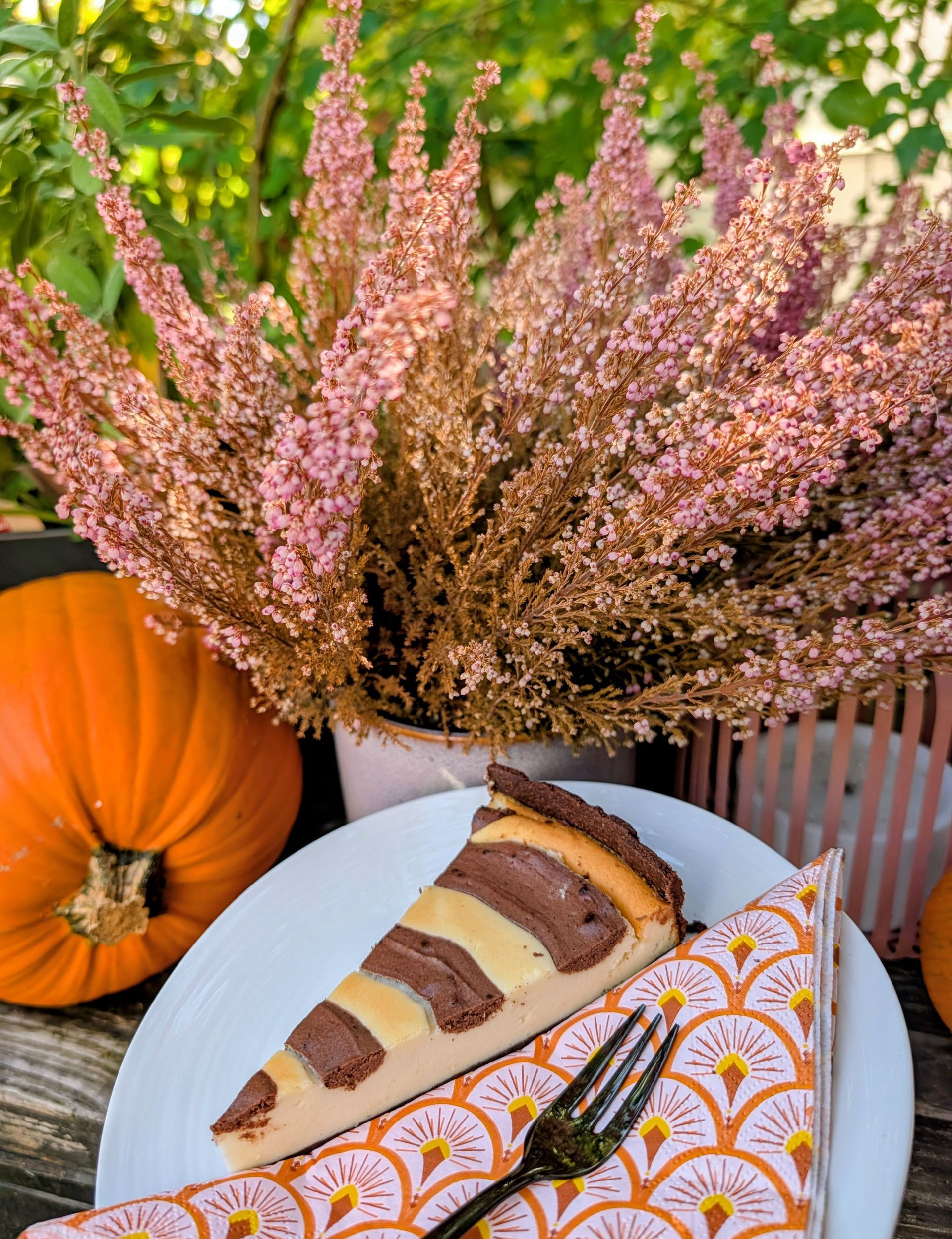 Kuchenteller mit Cheesecake. Im Hintergrund ein Kürbis und eine Blume.