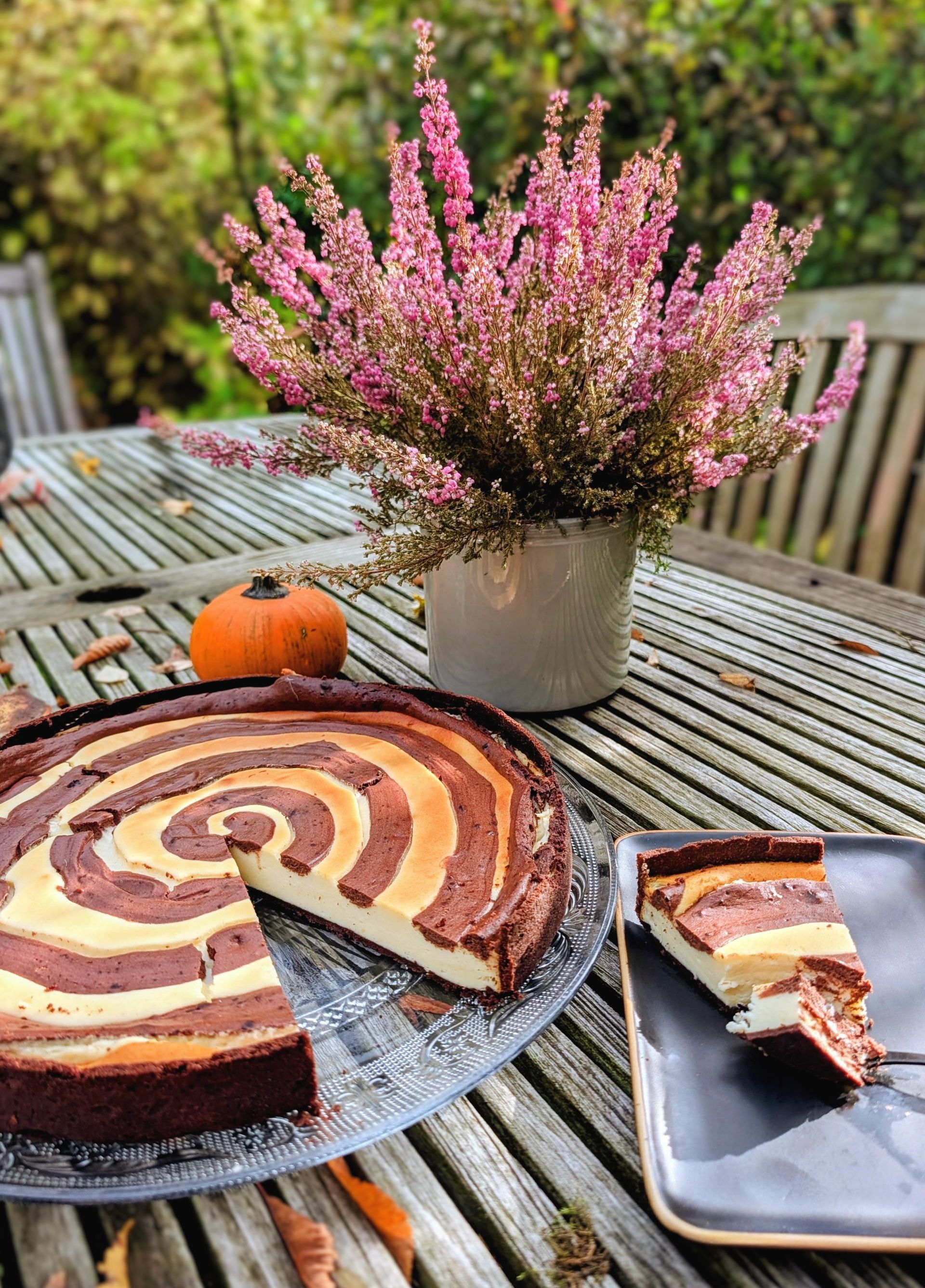 Holztisch mit einem Kuchen, einem kleinen Kürbis und einer Blume darauf.