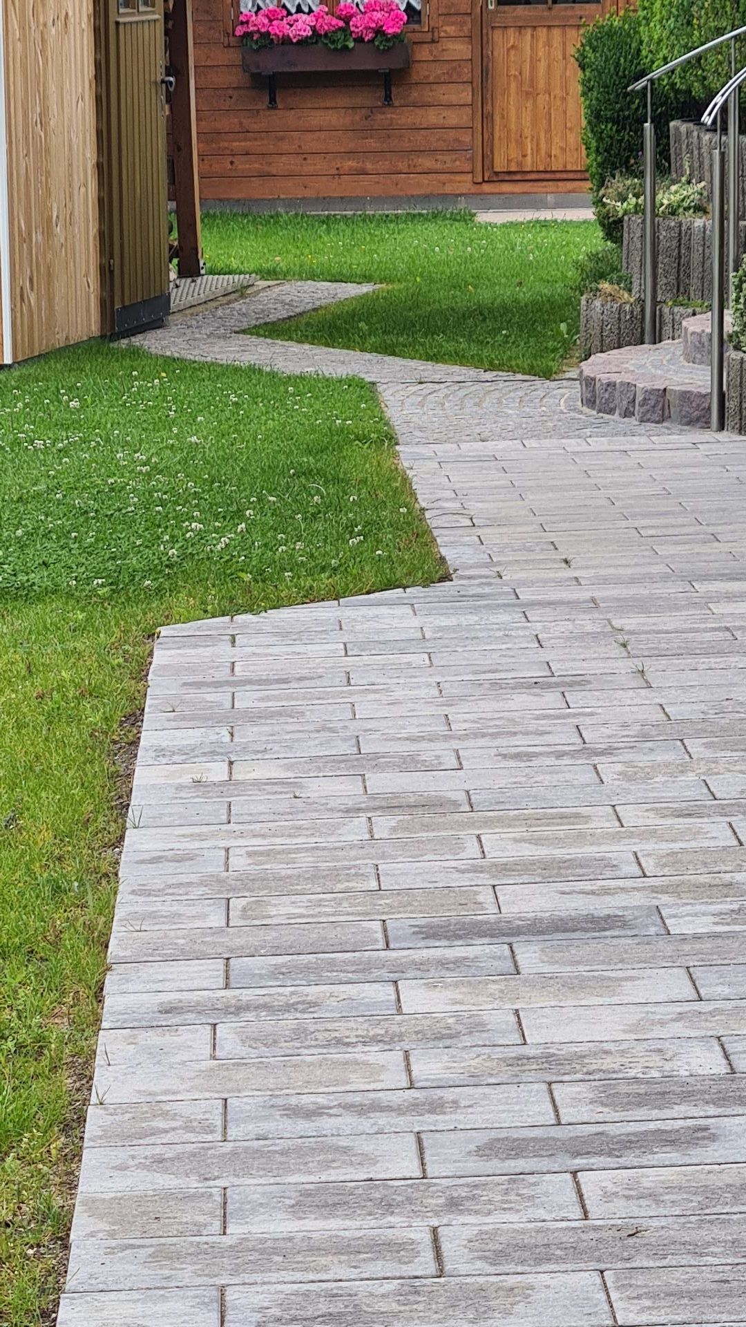 Ein gemauerter Gehweg führt zu einem Haus mit einem Holzschuppen im Hintergrund