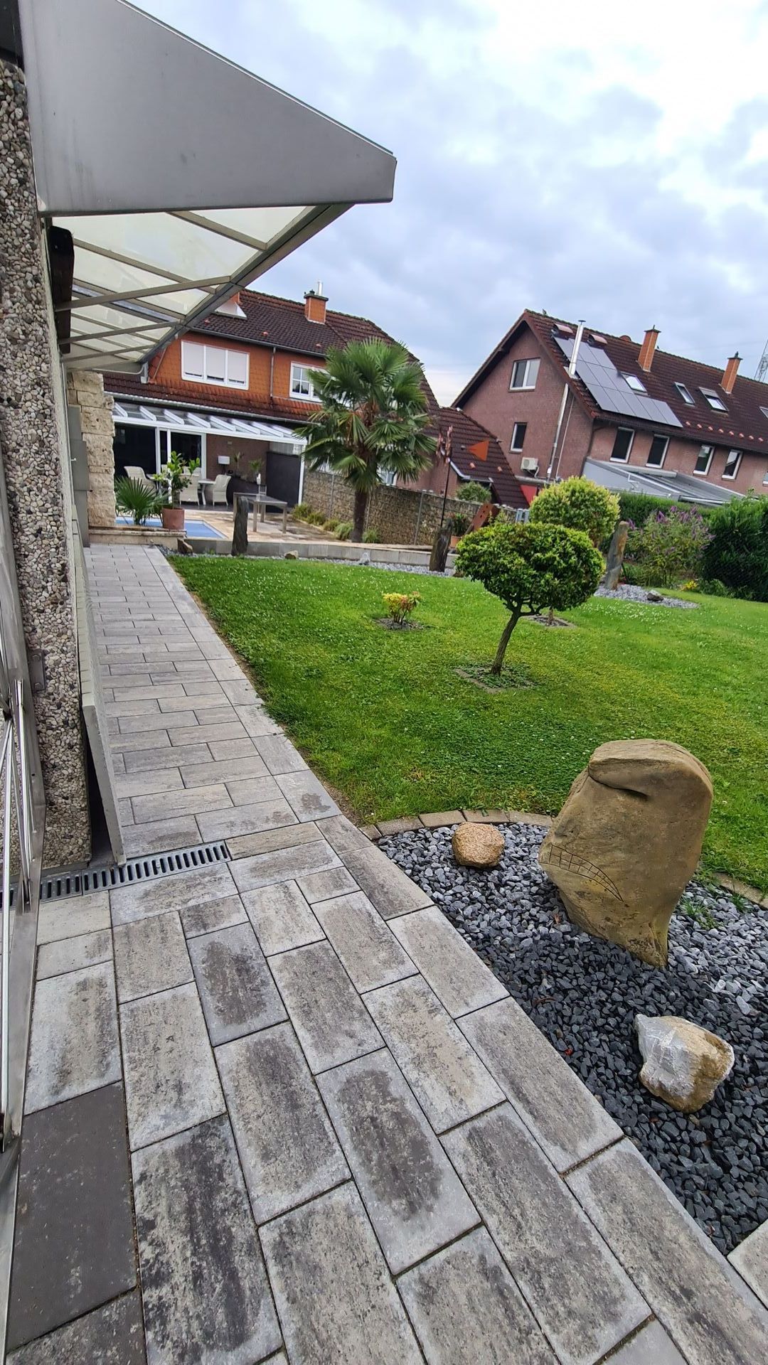 Ein gemauerter Gehweg führt zu einem üppig grünen Hof mit Häusern im Hintergrund
