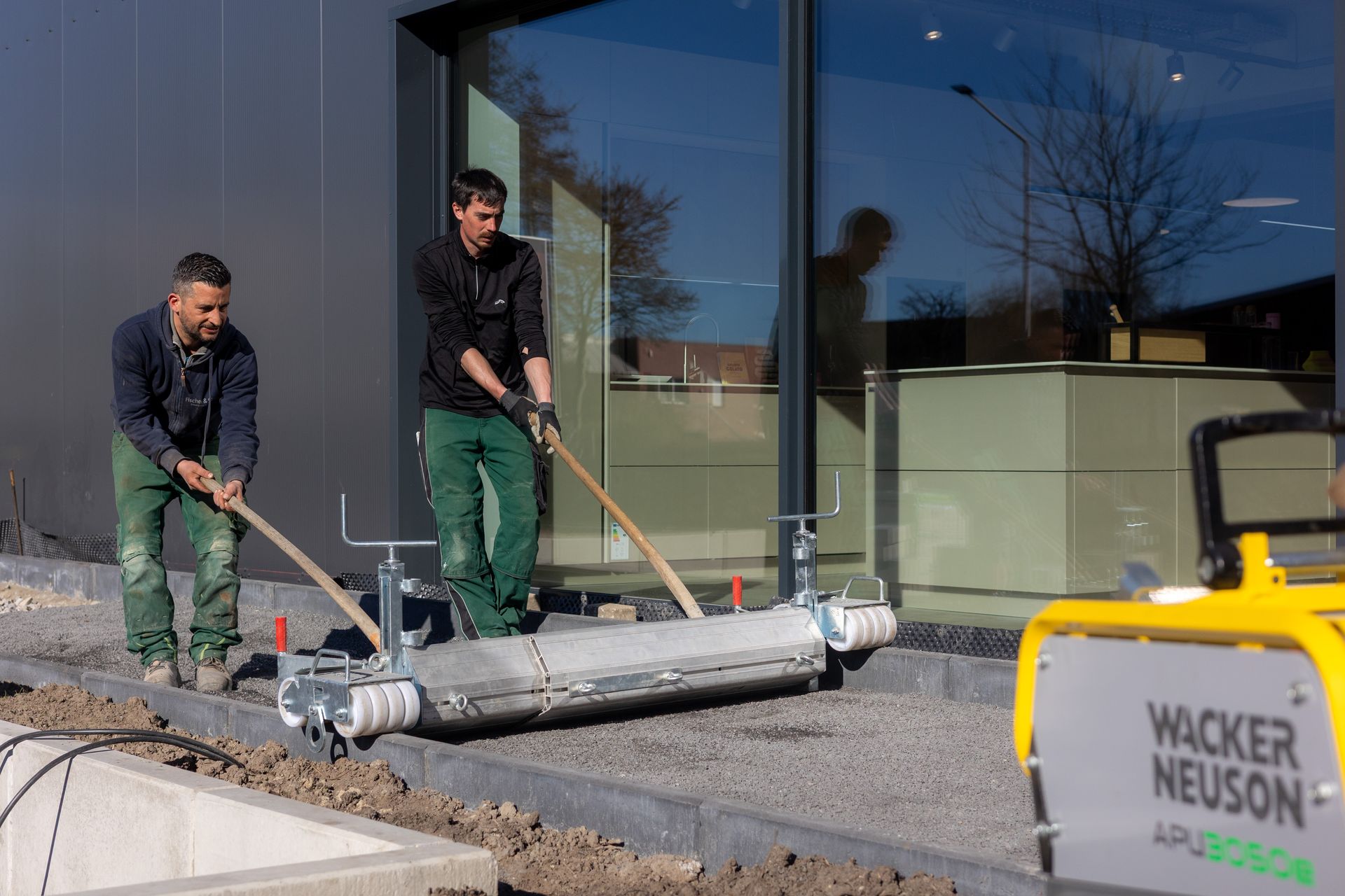 Zwei Männer arbeiten auf einem Gehweg vor einem Gebäude