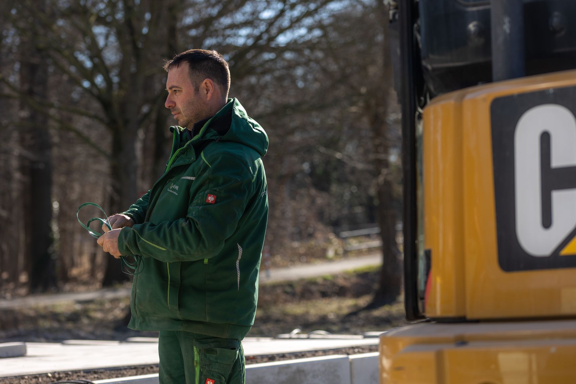 Ein Mann in einer grünen Jacke steht neben einem gelben Cat-Bagger