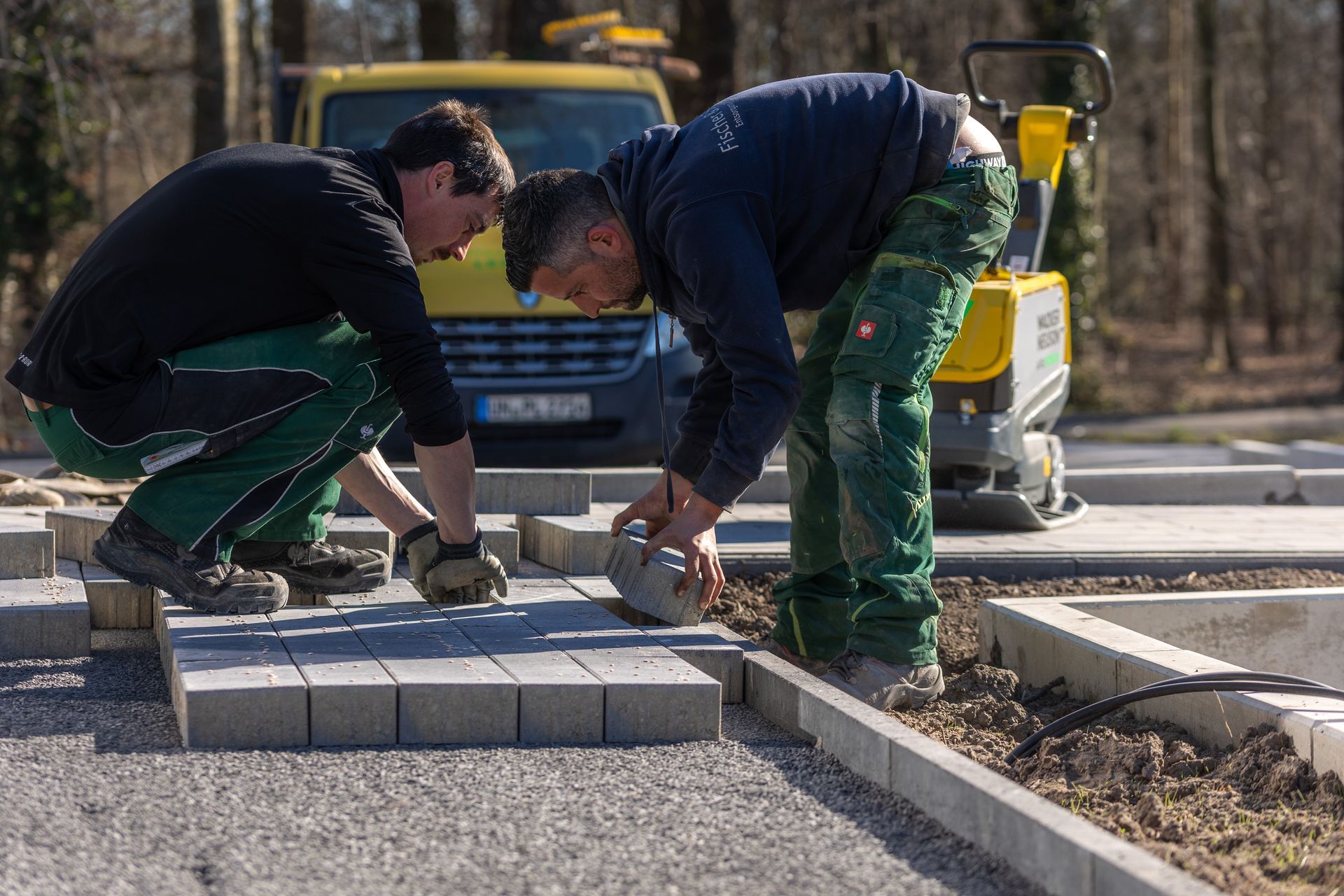 Zwei Männer arbeiten auf einem Bürgersteig vor einem gelben Lieferwagen